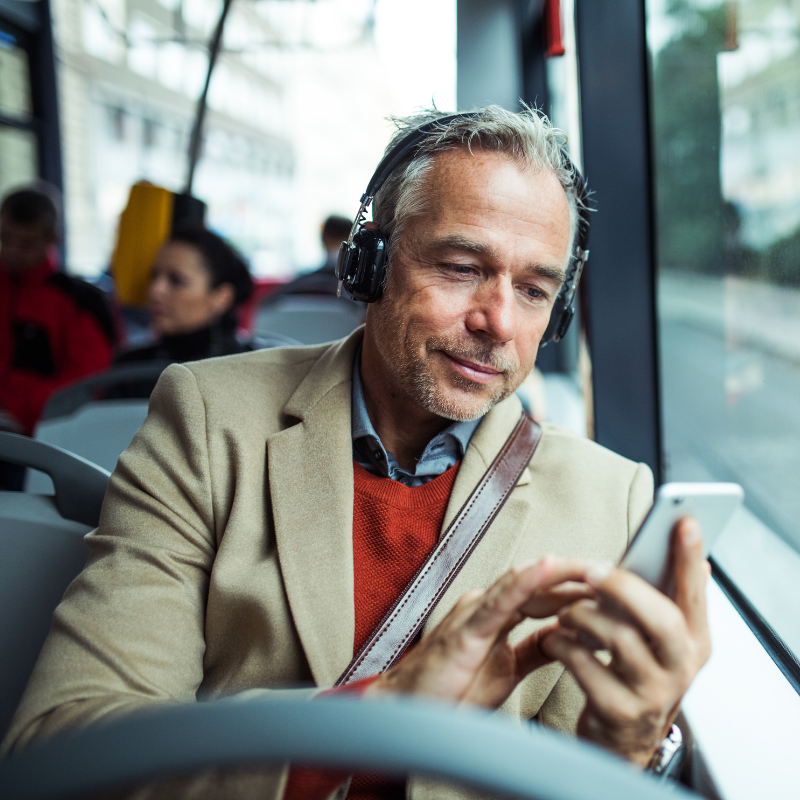 Mature tired businessman with heaphones and smartphone travelling by bus in city.